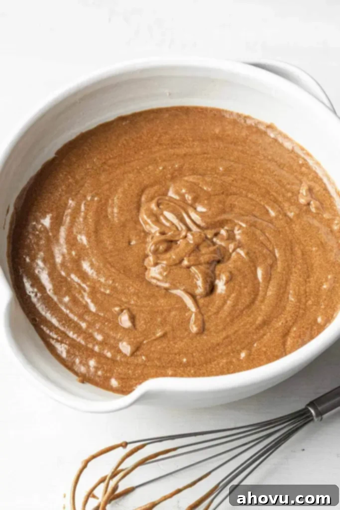Gingerbread cake batter in a large white mixing bowl. A batter-covered whisk rests on the side. 