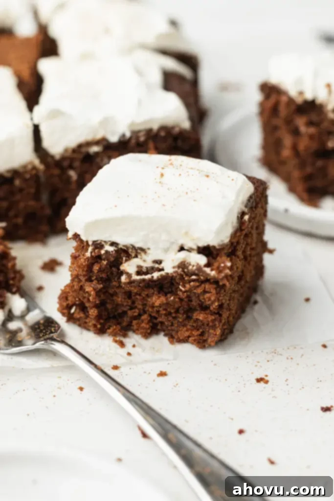 Slices of spiced molasses cake topped with whipped cream. A fork rests on the side. 