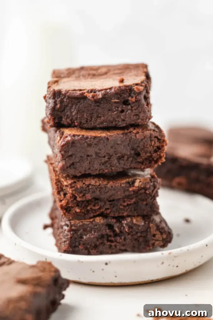 A stack of four rich, fudgy cocoa powder brownies on a clean white dessert plate, ready for enjoyment. 