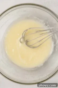 An overhead view of a perfectly melted butter-sugar mixture being whisked in a clear glass mixing bowl, reflecting the light.