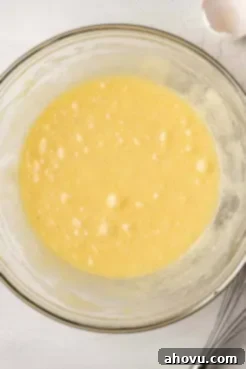 An overhead view of the combined wet ingredients, including melted butter, sugar, eggs, and vanilla, in a clear glass mixing bowl, beautifully blended.