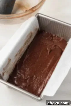 Small batch brownie batter smoothly spread into a parchment paper-lined loaf pan, ready for the oven to create delicious fudgy brownies.