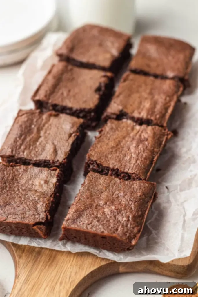 Eight perfectly sliced, rich, fudgy brownies arranged neatly on a parchment-lined wood serving board, inviting a bite. 