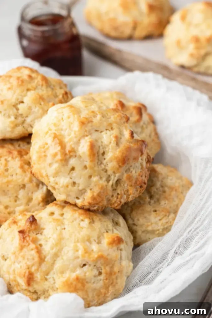 No-Fuss Fluffy Biscuits 2 A pile of homemade drop biscuits in a bowl, with a jam jar in the background, showcasing their golden-brown tops and rustic charm.