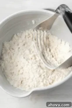 An overhead close-up view of cold butter being cut into a mixture of flour and other dry ingredients using a pastry cutter, essential for flaky biscuits.