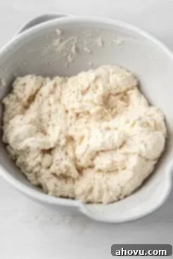 An overhead view of the shaggy, mixed dough for drop biscuits in a stainless steel mixing bowl, ready for scooping.