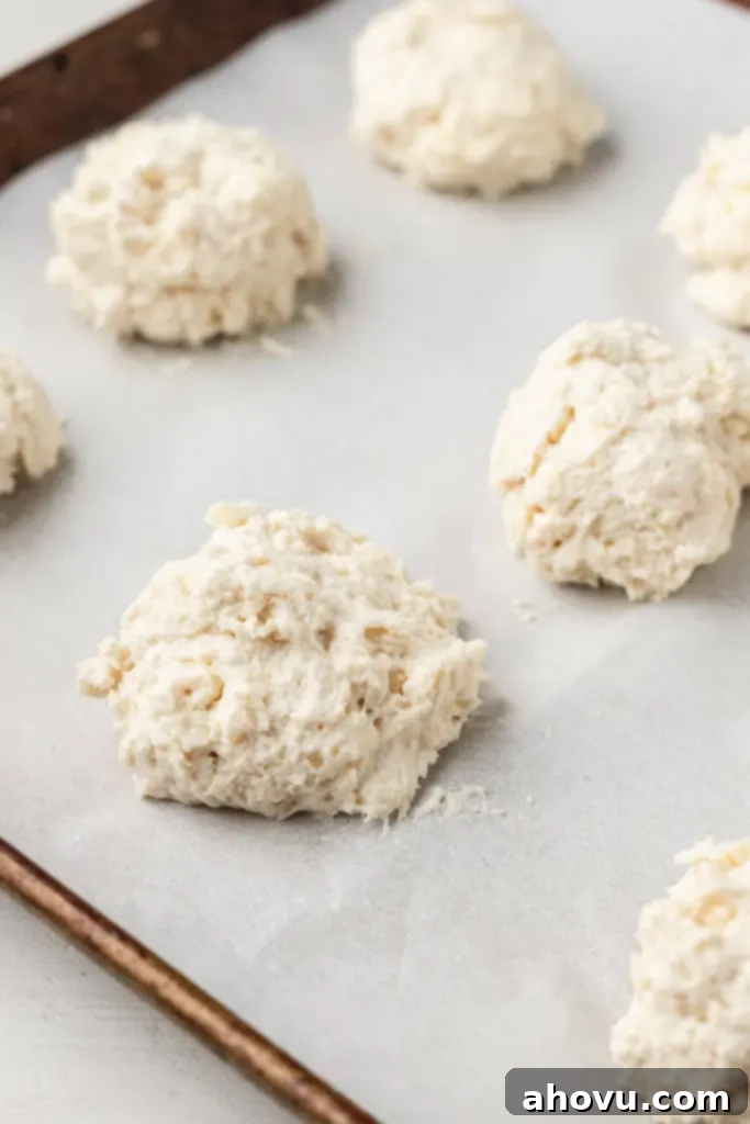 No-Fuss Fluffy Biscuits 4 A parchment-lined baking sheet dotted with mounds of freshly scooped drop biscuit dough, evenly spaced and ready for baking.
