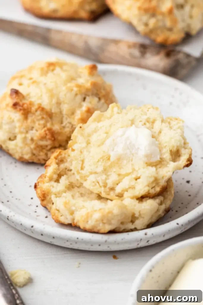 No-Fuss Fluffy Biscuits 6 Two drop biscuits on a white plate. One biscuit is whole, and the other has been cut in half and generously topped with melting butter.