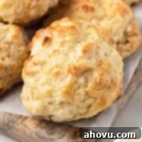 No-Fuss Fluffy Biscuits 8 Several golden-brown drop biscuits on top of a wooden cutting board with a piece of parchment paper, ready to be served.