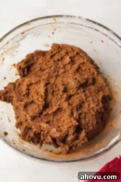Freshly mixed, rich brown gingerbread cookie dough resting in a glass mixing bowl, ready for chilling.