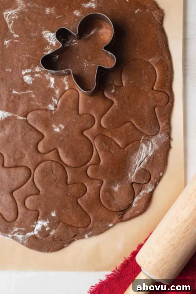 An overhead shot of gingerbread cookie dough being meticulously cut out with a star-shaped cookie cutter on parchment paper, ready for baking.
