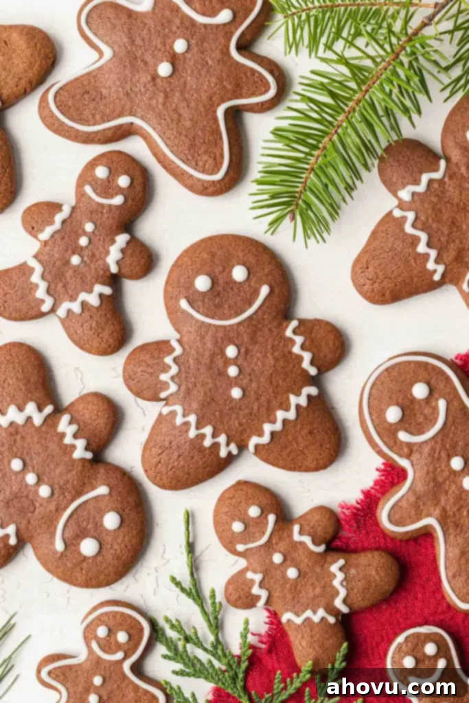 A beautiful overhead display of festive homemade gingerbread cookies, artfully decorated with white icing, surrounded by sprigs of pine, creating a charming holiday scene.