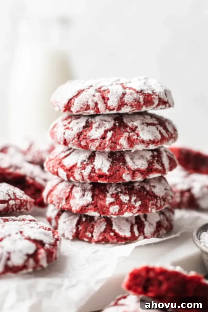 A stack of five red velvet crinkle cookies, with more cookies scattered around the base. 