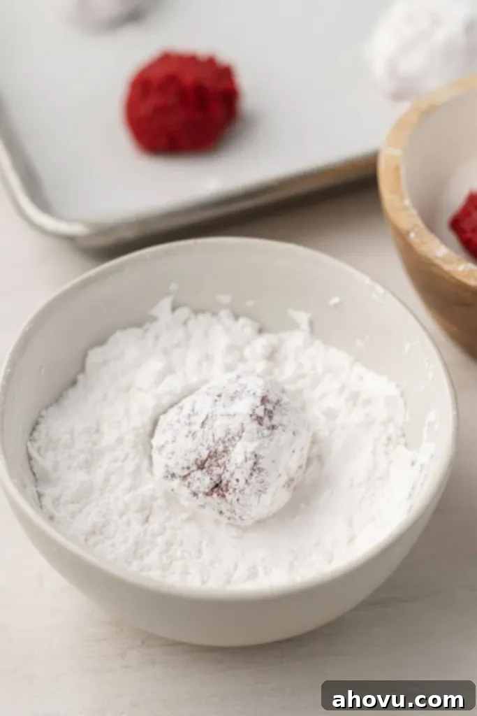 A red velvet cookie dough ball being rolled in powdered sugar. 