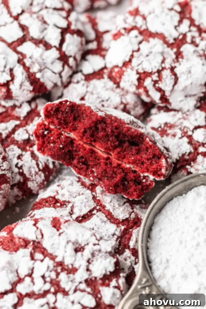 A close up view of a red velvet cookie that's been broken in half and stacked on itself, amidst a pile of cookies. 
