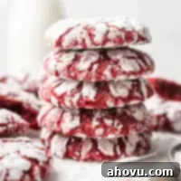 A stack of four red velvet crinkle cookies. More cookies and a small jug of milk are in the background.