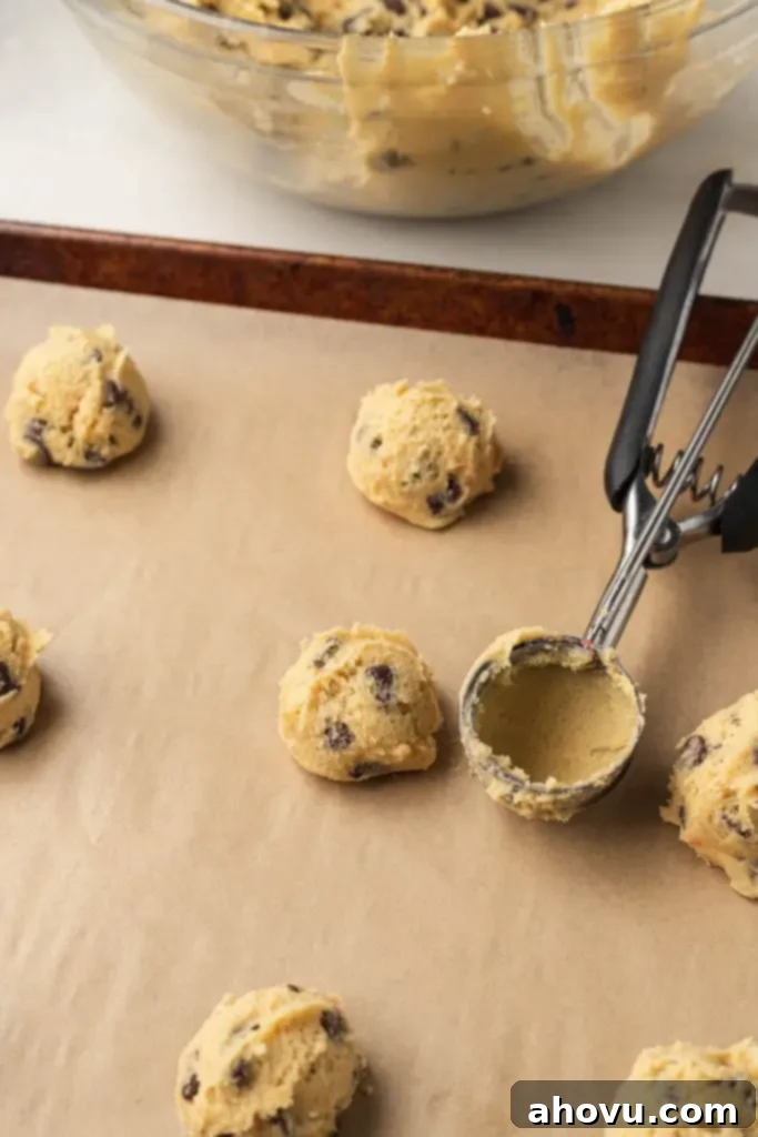 Chocolate chip cookie dough balls on a parchment-lined baking sheet, with a used cookie scoop. 