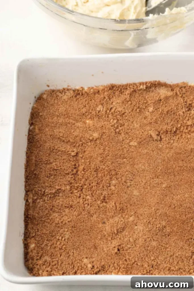 Glazed Cinnamon Honey Bun Cake 5 A process shot of cinnamon sugar filling in a white baking dish. A bowl of cake batter is in the background.