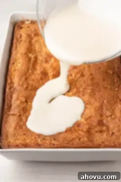 A process shot showing vanilla icing being poured over a baked cinnamon swirl cake.
