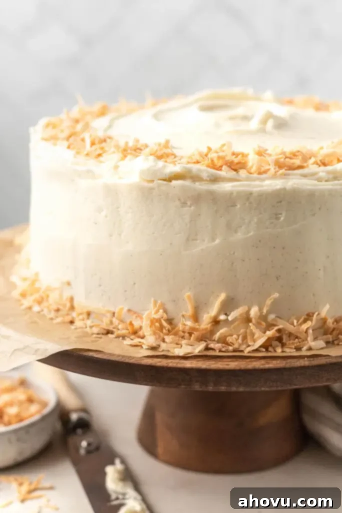 Tropical Coconut Dream Cake 2 A coconut cake with coconut buttercream frosting and toasted coconut on a wooden cake stand.