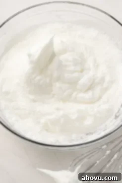 A glass mixing bowl with egg whites that have been beaten to stiff peaks.