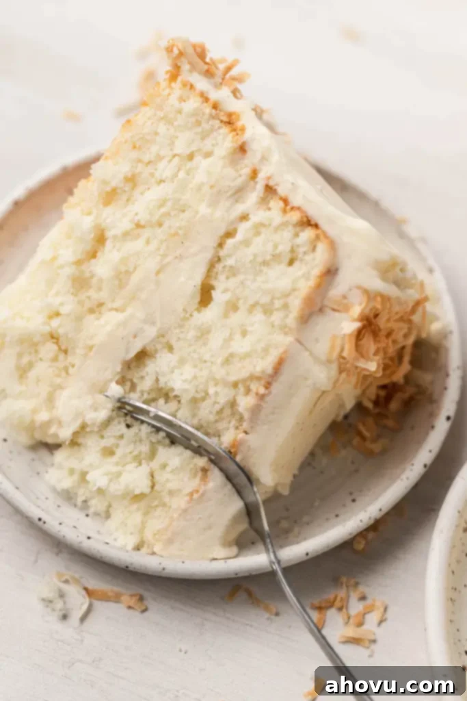 Tropical Coconut Dream Cake 6 A piece of frosted coconut layer cake on a white speckled dessert plate with a fork.