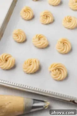 Piped butter cookie dough on a parchment-lined baking heet. A piping bag rests on the side.