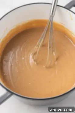 Rich, golden caramel filling being whisked in a saucepan over medium heat, showing its thick, creamy consistency.