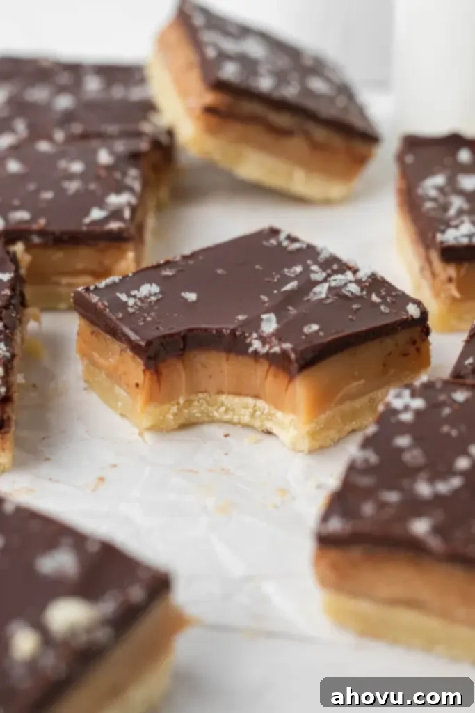Millionaire Shortbread 5 Millionaire shortbread bars on parchment paper, with one bar in the middle showing a bite missing, highlighting its delicious layers.