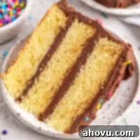 A slice of yellow cake on a white speckled plate.