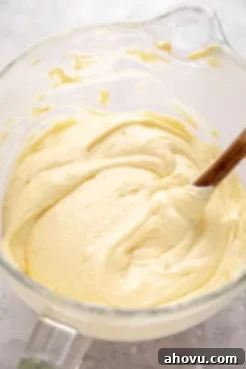 A glass mixing bowl showing yellow cake batter after the whipped egg whites have been gently folded in, creating a lighter, airy texture ready for baking.