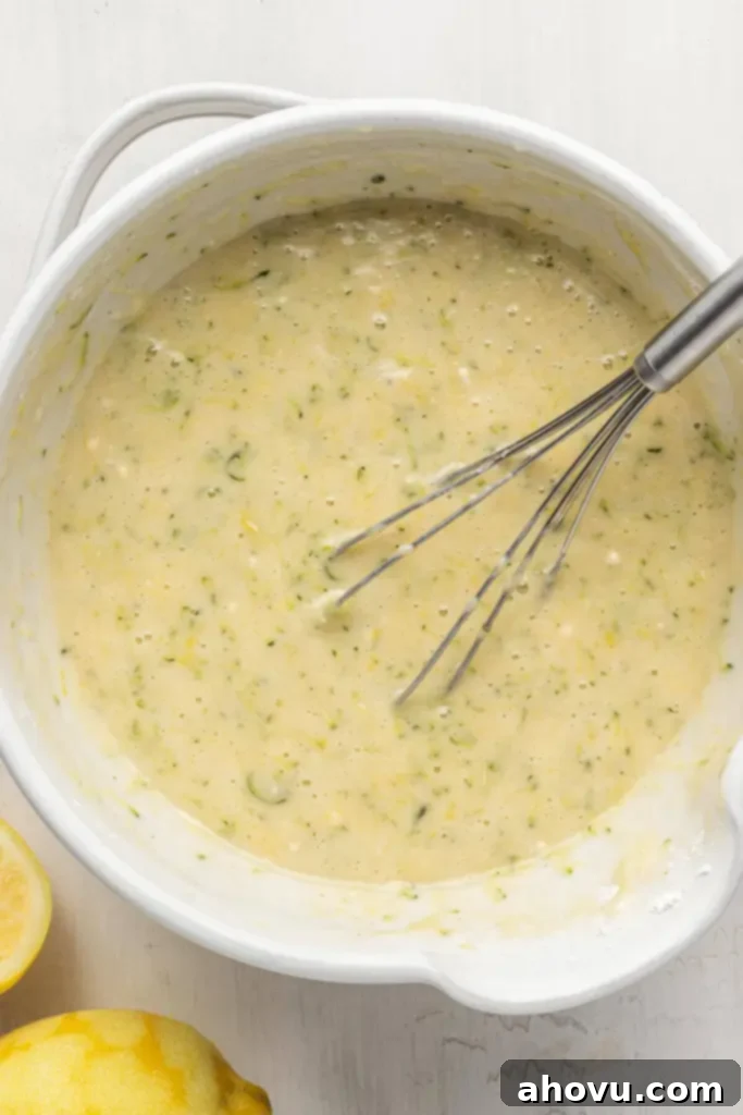 An overhead view of zucchini bread batter in a white mixing bowl, with a whisk.