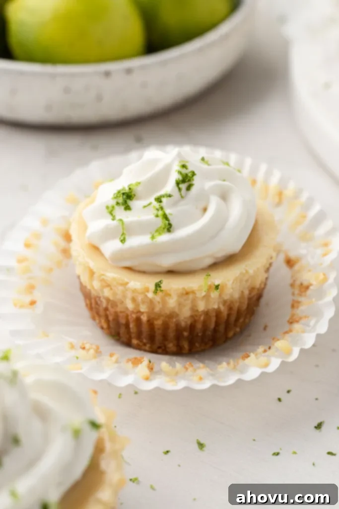 A mini key lime pie, with the muffin liner pulled down. A bowl of key limes is sitting in the background.