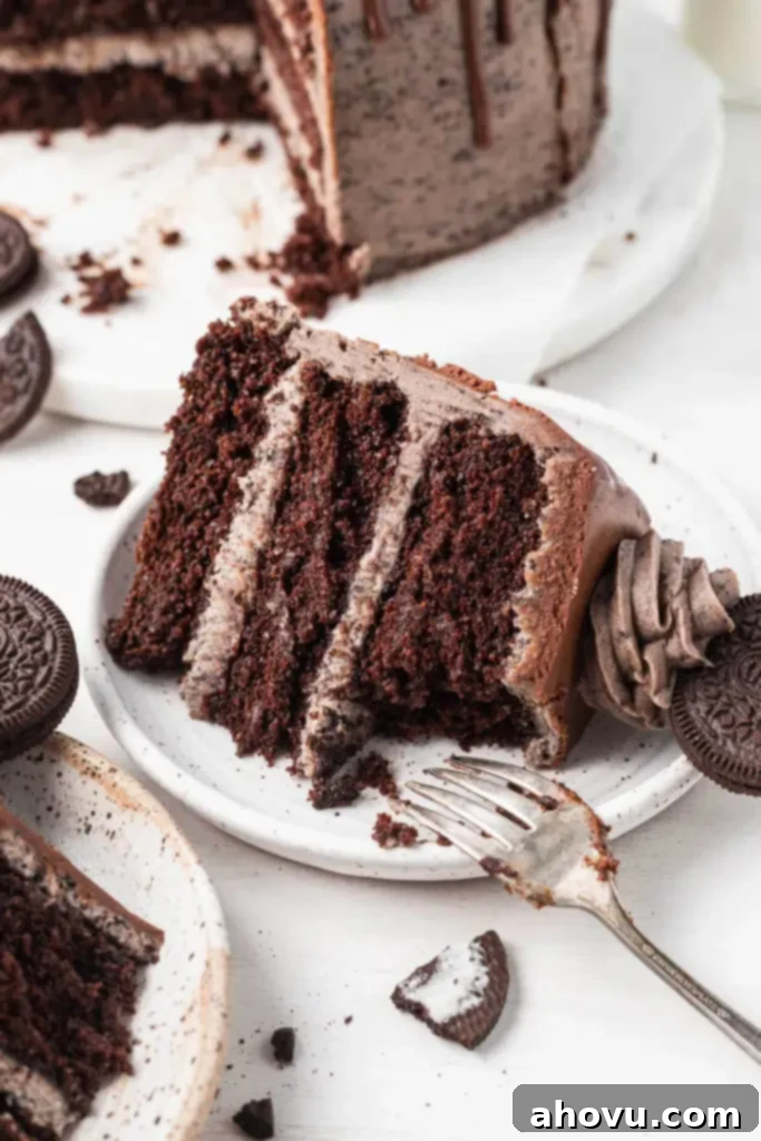Decadent Oreo Cake 7 A delectable slice of Oreo cake on a white dessert plate, with a small bite missing, emphasizing its deliciousness and inviting taste. The visible layers of rich chocolate cake and creamy Oreo frosting are enticing.