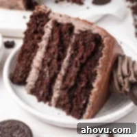 Decadent Oreo Cake 8 A delightful slice of Oreo cake, featuring moist chocolate layers and rich Oreo buttercream, presented on a white speckled plate.