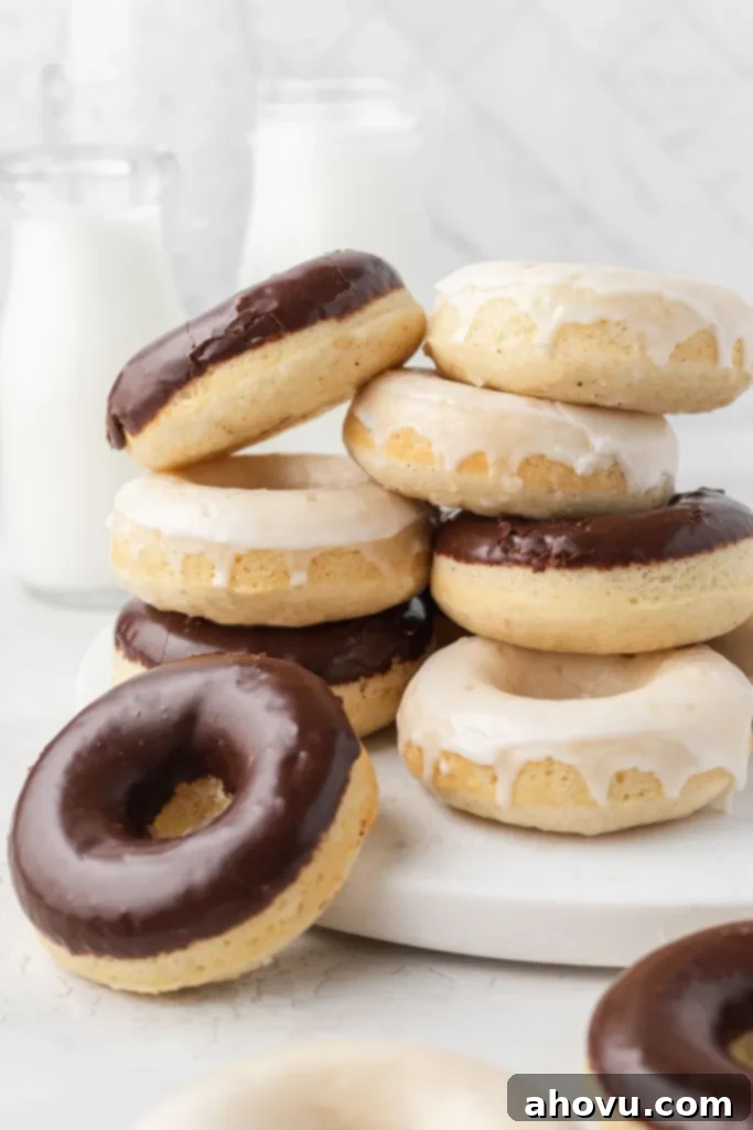 Two enticing stacks of freshly baked donuts, one generously topped with smooth vanilla icing and the other with decadent chocolate icing, inviting you to indulge.