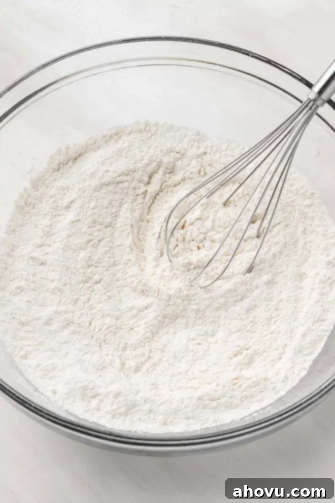 An overhead view of the dry ingredients for baked donuts, including flour, sugar, and spices, combined in a glass mixing bowl.