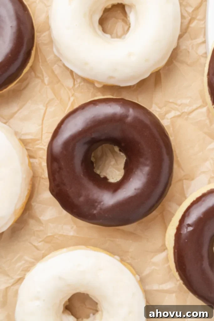 An overhead view of freshly baked donuts glistening with delicious icing, neatly arranged on a piece of parchment paper.