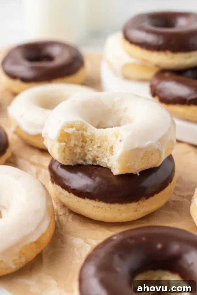 Several moist baked cake donuts neatly arranged on parchment paper, with two perfectly stacked in the center, showcasing their soft texture.