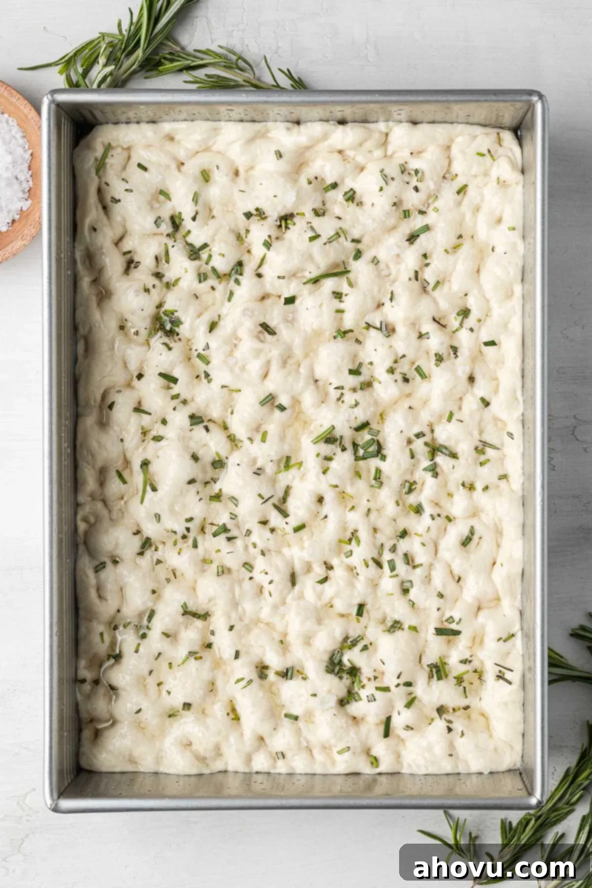An overhead view of raw focaccia dough in a metal baking pan. 