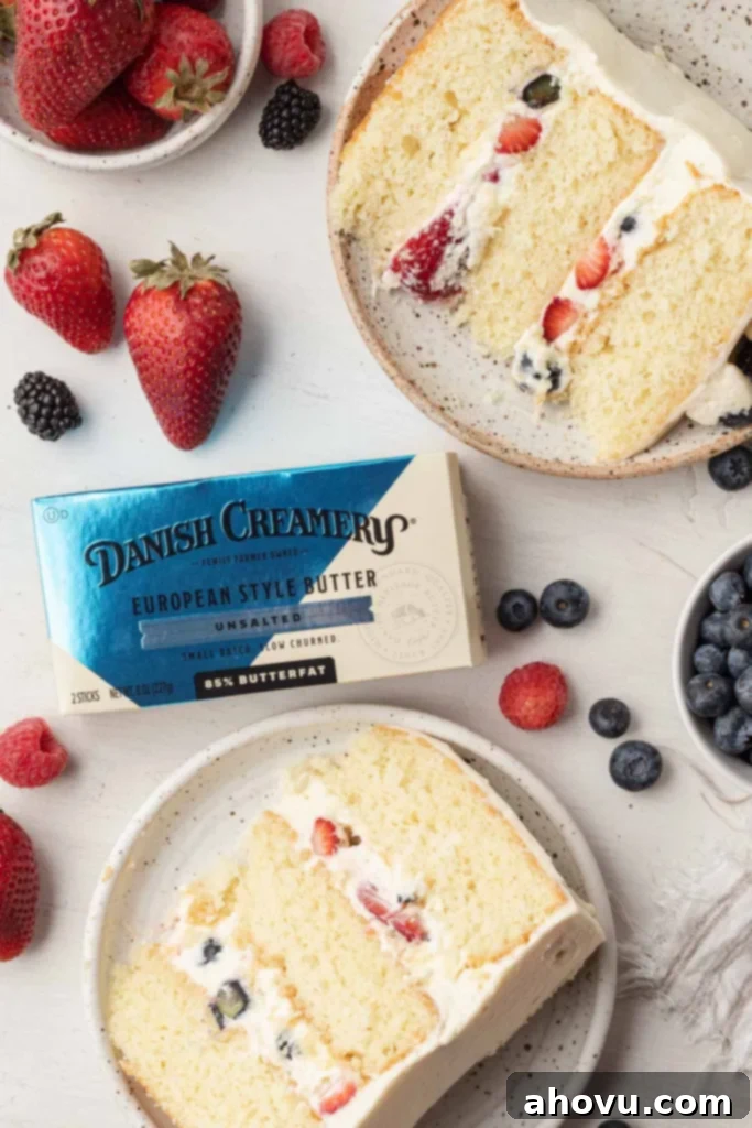 An overhead view of two slices of Chantilly cake on speckled dessert plates, with a package of Danish Creamery butter between them.