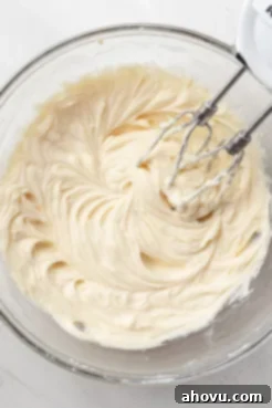An overhead view of cream cheese being beaten in a glass mixing bowl.