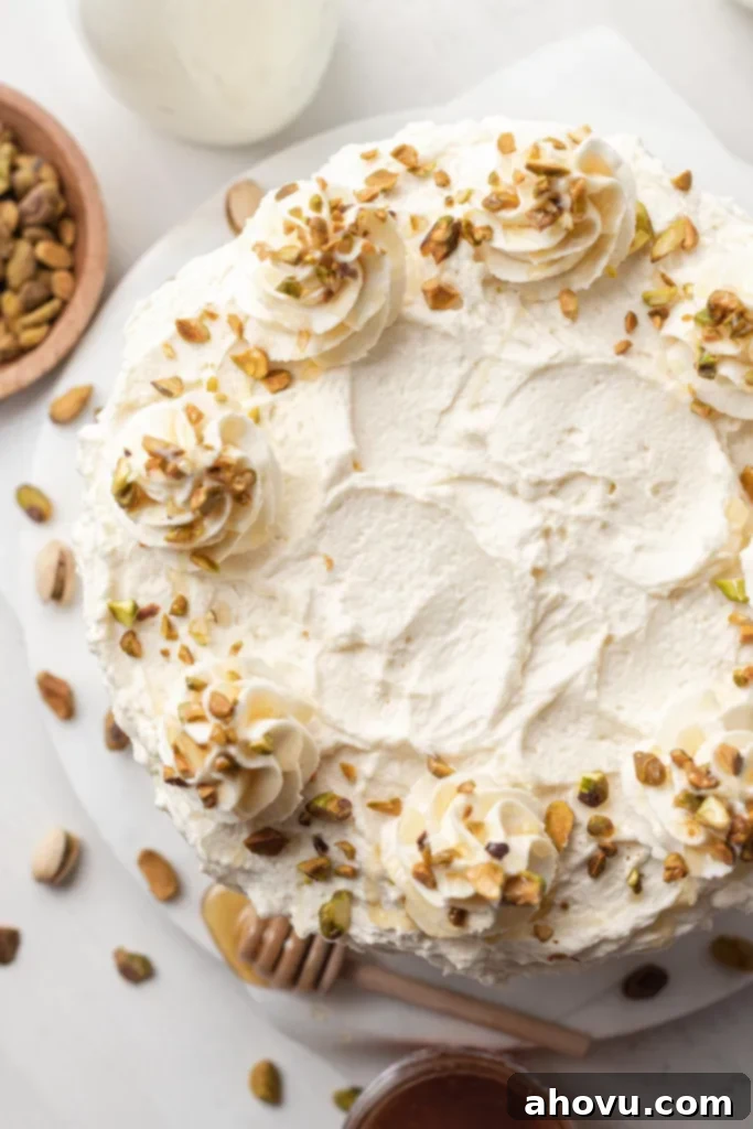 An overhead view of a frosted pistachio cake, with pistachios and honey on the side. 
