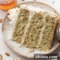A slice of pistachio cake on a speckled plate. A small jar of honey and pistachios are near the plate.