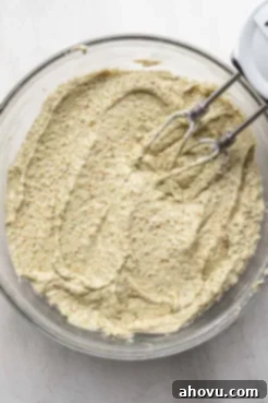 An overhead view of pistachio cake batter with electric beaters in a glass mixing bowl.
