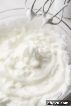 Whipped egg whites with electric beaters in a glass bowl.