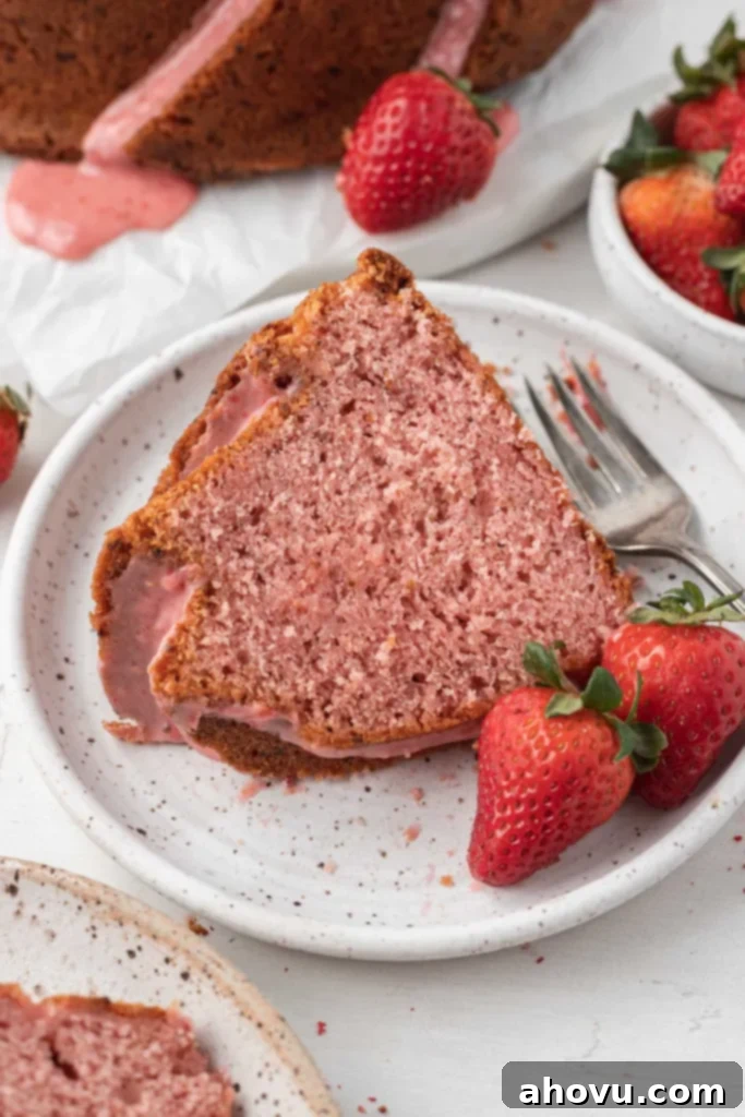 A slice of strawberry glazed pound cake on a white dessert plate with fresh berries and a fork. 