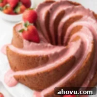 A strawberry pound cake topped with strawberry icing. A few strawberries rest on top of the cake.