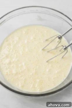 Sponge cake batter in a glass mixing bowl, with metal beaters leaning on the side.