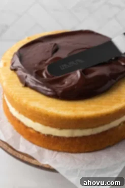 Chocolate ganache being spread over a homemade Boston cream pie cake.